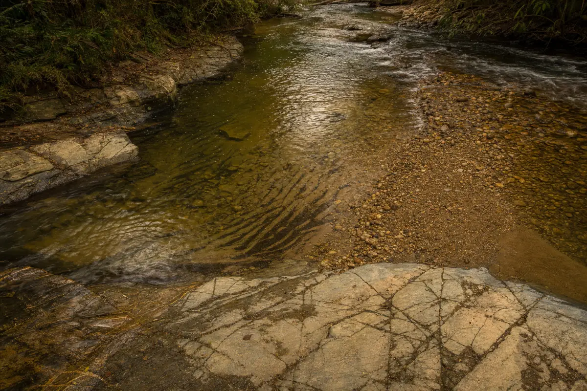 Trecho raso de rio com bedrock fraturado, corrente, cascalho e faixas de minerais pesados